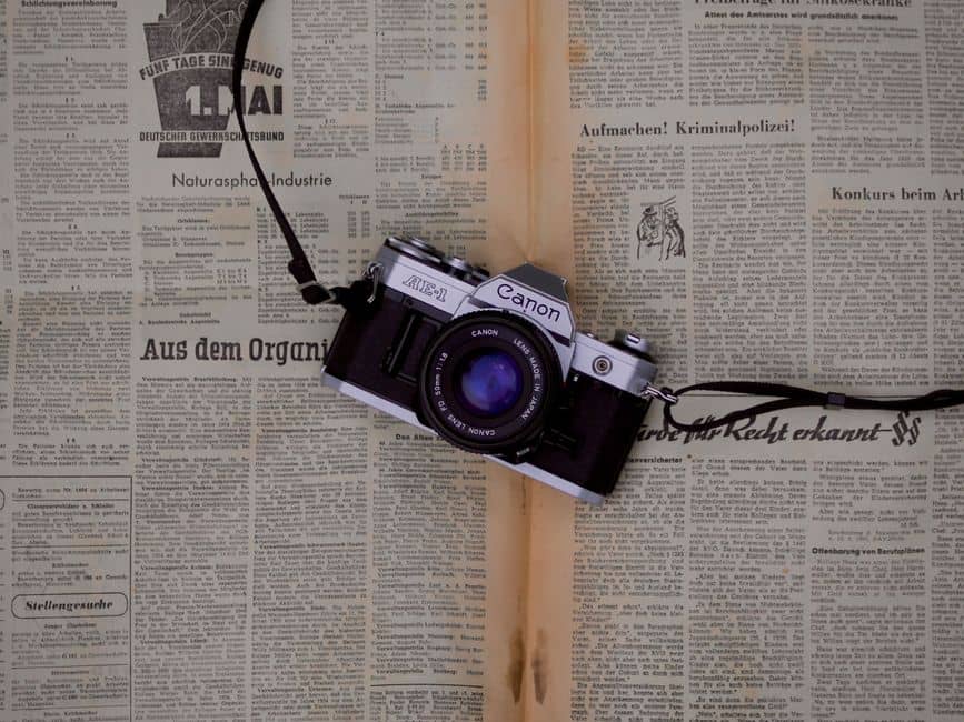 Classic Canon AE-1 film camera resting on vintage newspaper surface.