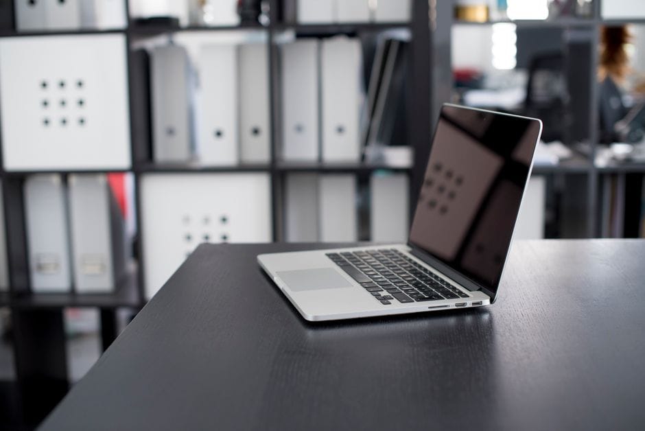 MacBook Pro displayed on a minimalist office desk with shelves in the background.