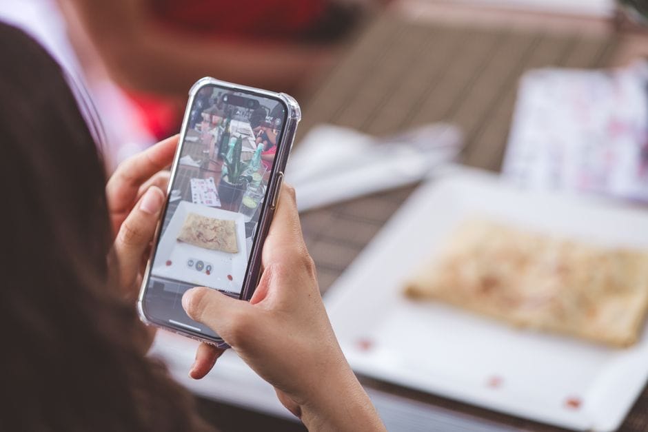 Close-up of a woman photographing a meal at a restaurant using a smartphone.