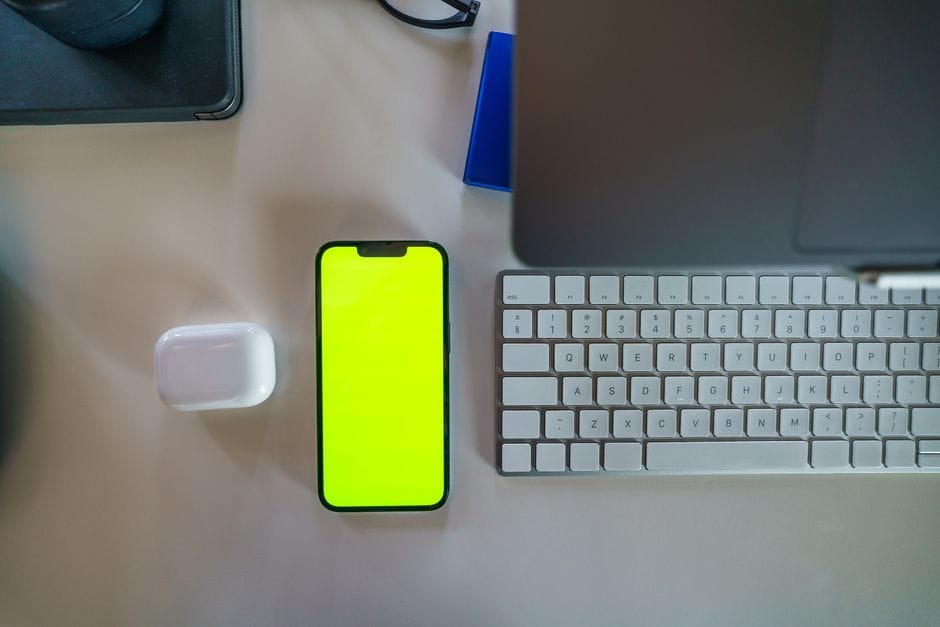 Top-down view of a modern workspace featuring a smartphone with a green screen, laptop, and keyboard.