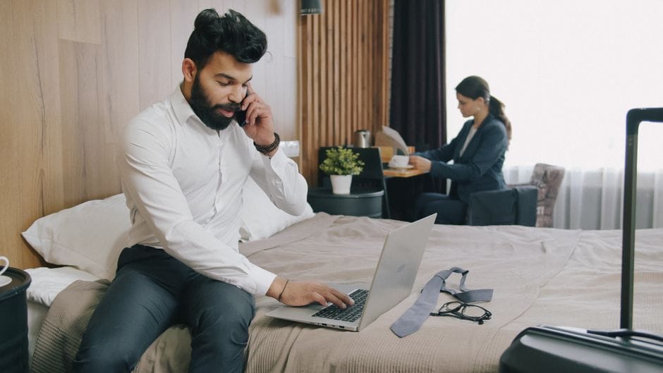 Two business professionals multitasking in a hotel room, focusing on calls and documents.