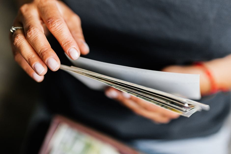 A detailed view of an adult's hands flipping through various papers indoors.