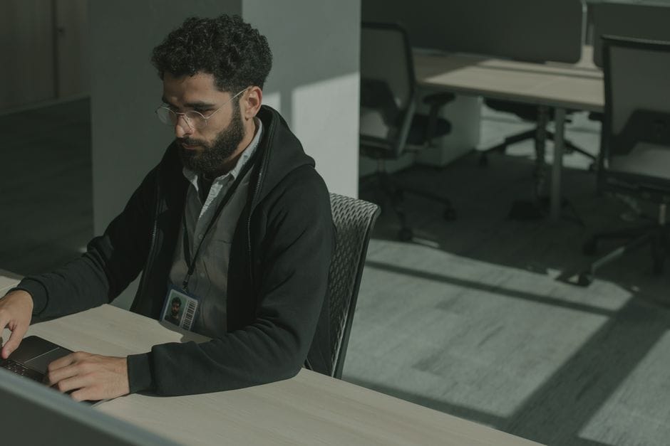 Bearded man working on a computer indoors, focused on cybersecurity tasks.