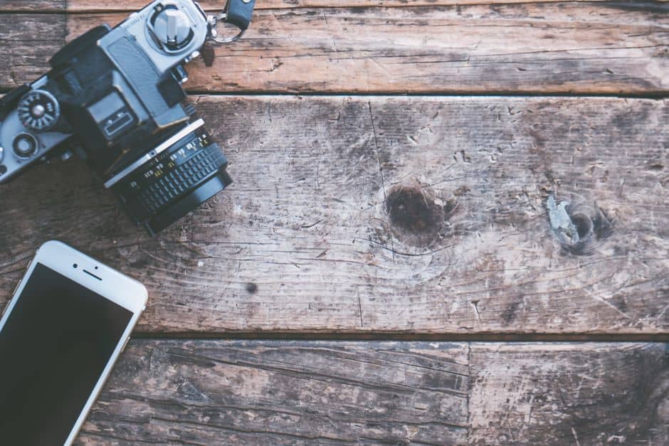 A vintage camera and smartphone on a rustic wooden surface, highlighting technology contrast.
