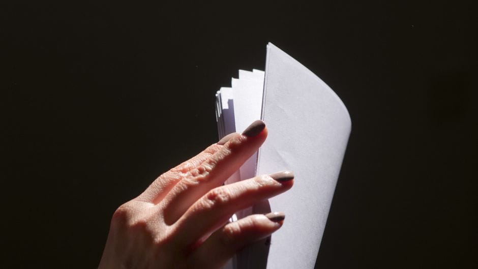 Close-up of a hand flipping through a stack of papers against a dark background.