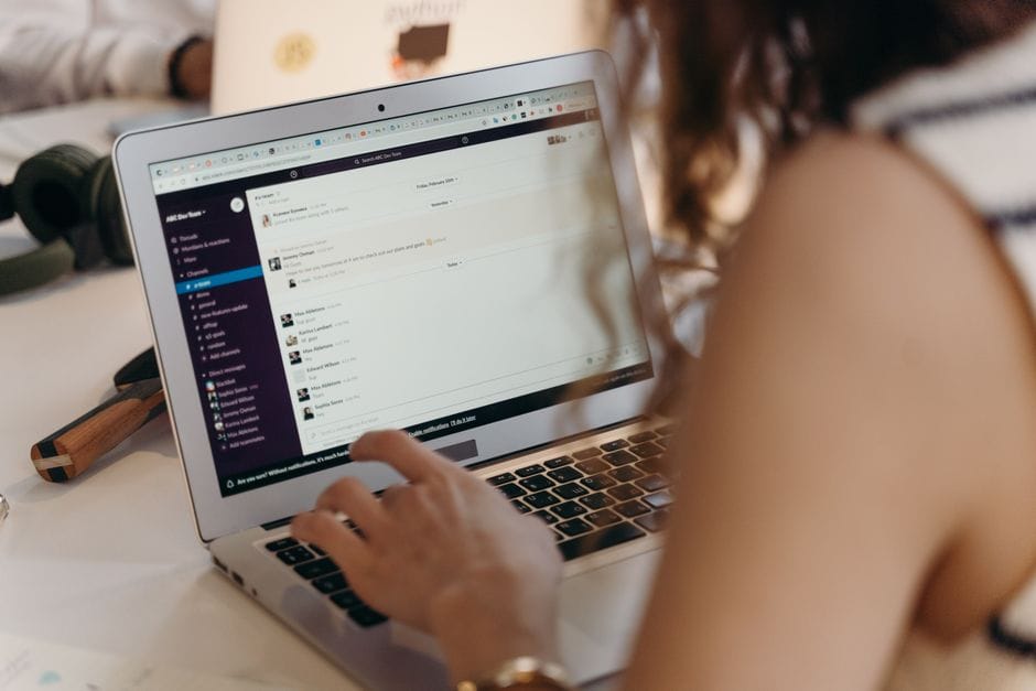 A businesswoman typing on a laptop in an office setting, using Slack for communication.