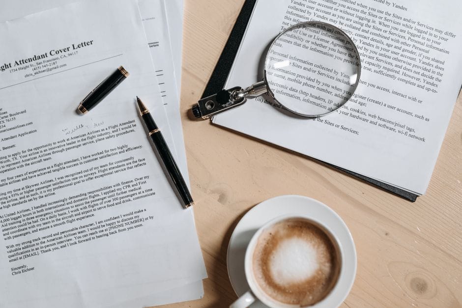 How to Merge Two PDF Files Into One for Free A top view of coffee and job application documents with a magnifying glass on a wooden desk.
