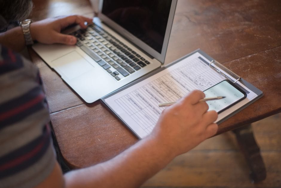 Why PDF to Word Conversion Loses Formatting (and How to Deal With It) Close-up of a person using a laptop and reviewing documents with a smartphone on a wooden table.