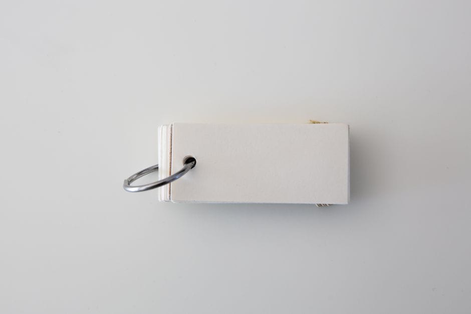 Top view of a minimalist white paper stack fastened with a metal ring against a white background.