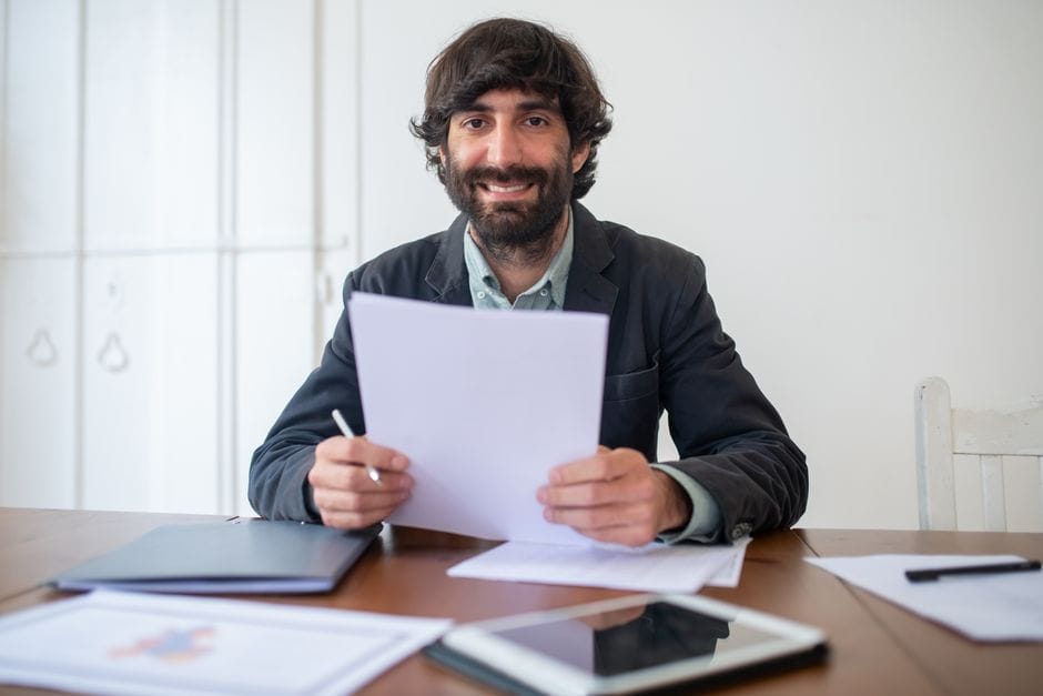 How to Rotate PDF Pages Permanently (Not Just in Your Viewer) Smiling businessman in a black jacket reviewing documents at his desk, indoors.